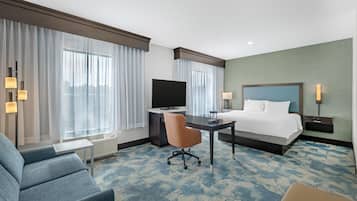 Une chambre d’hôtel équipée d’un lit, d’un bureau, d’une chaise, d’une télévision et d’une grande fenêtre avec des rideaux.