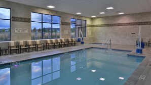 A swimming pool with chairs along the side, a lifeguard stand, and a view of the outdoors through large windows. - Hampton Inn & Suites Bend (Bend)