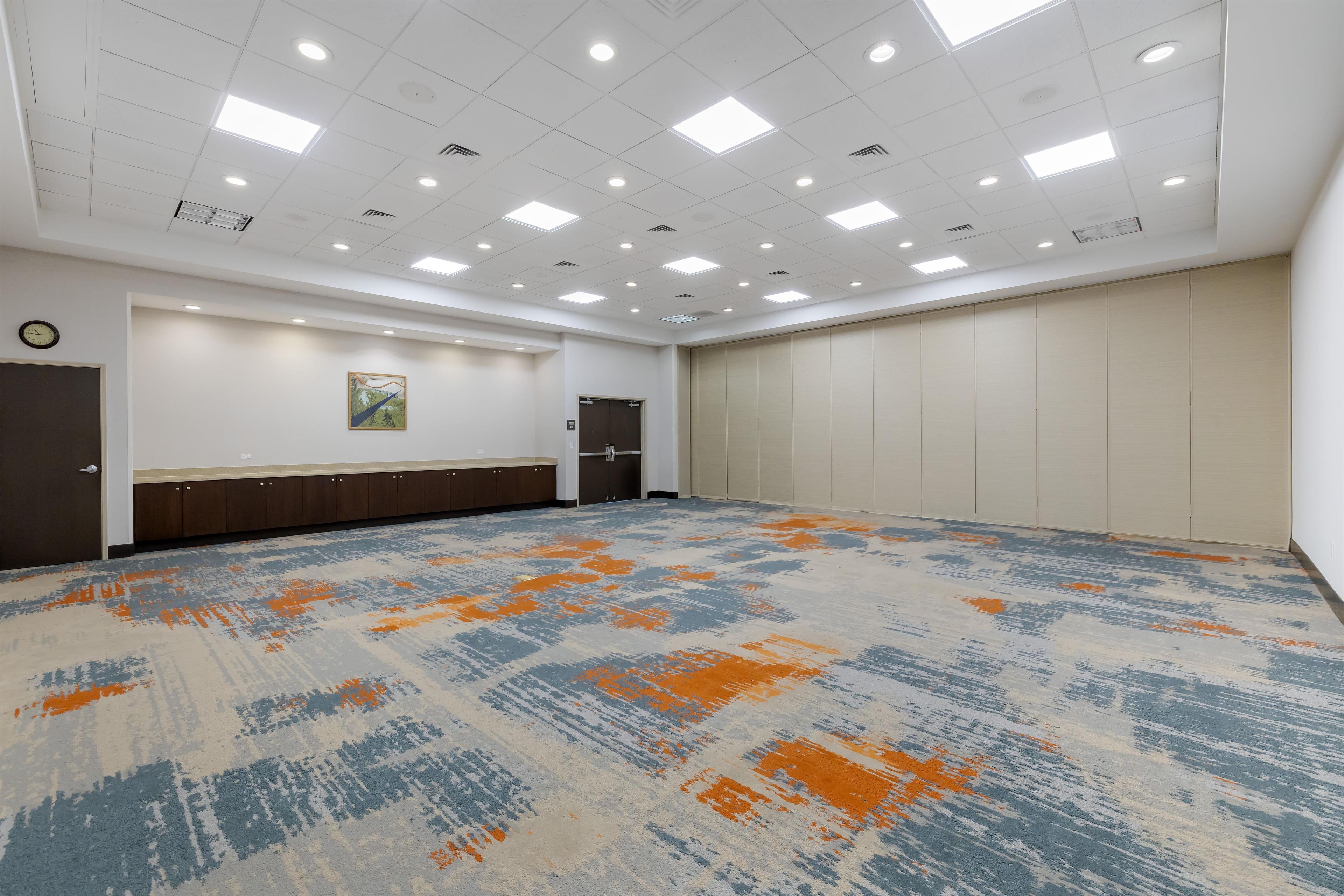 Un salón de conferencias con alfombra estampada, luces empotradas en el techo, un reloj y una puerta.