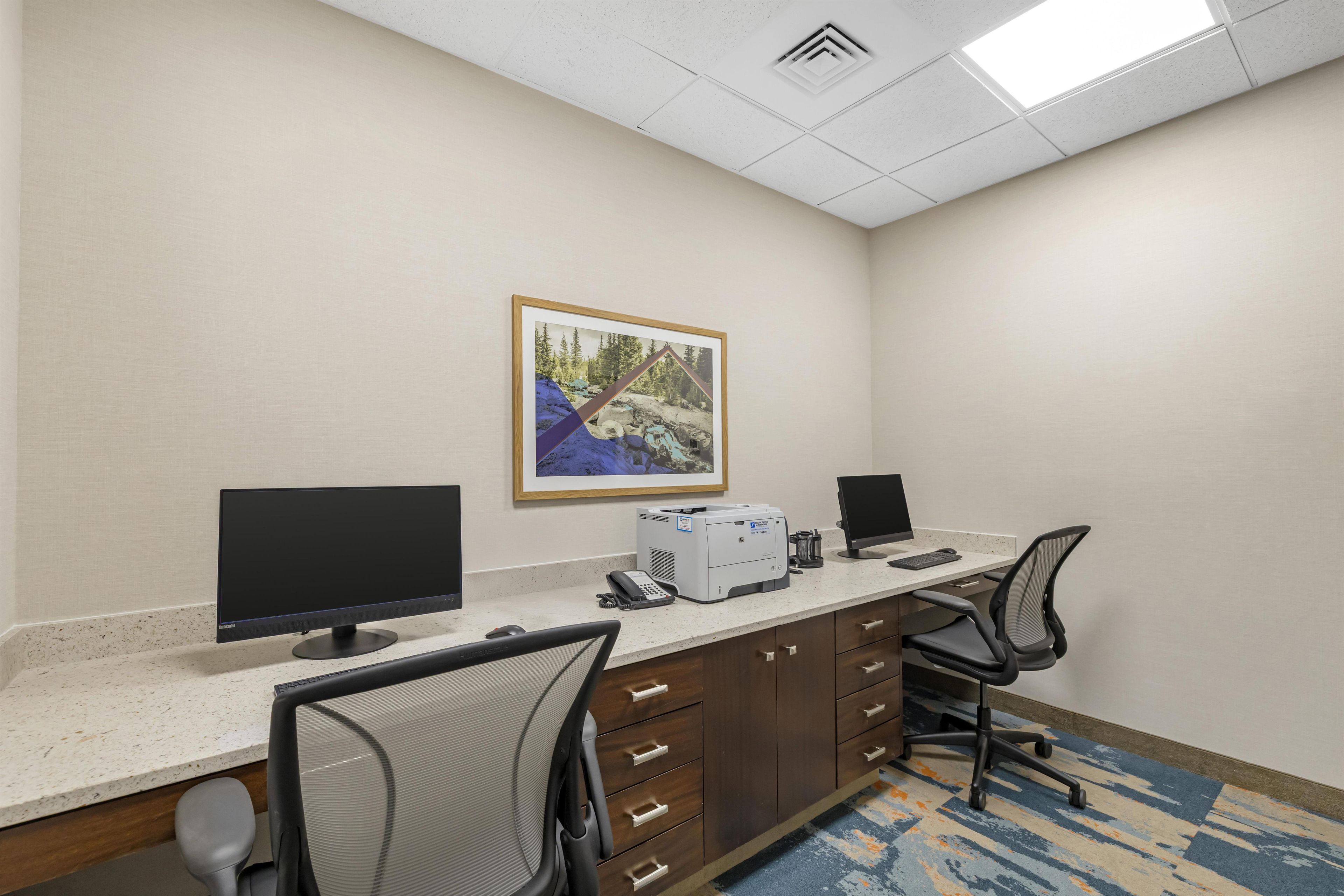 A hotel office with two desks, computers, chairs, a telephone, and a framed picture on the wall.