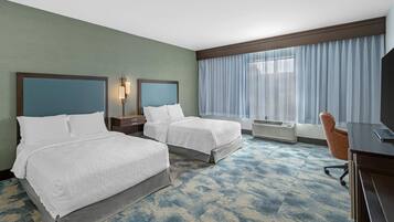 Habitación de hotel con dos camas, un escritorio, una silla y un ventanal con cortinas.