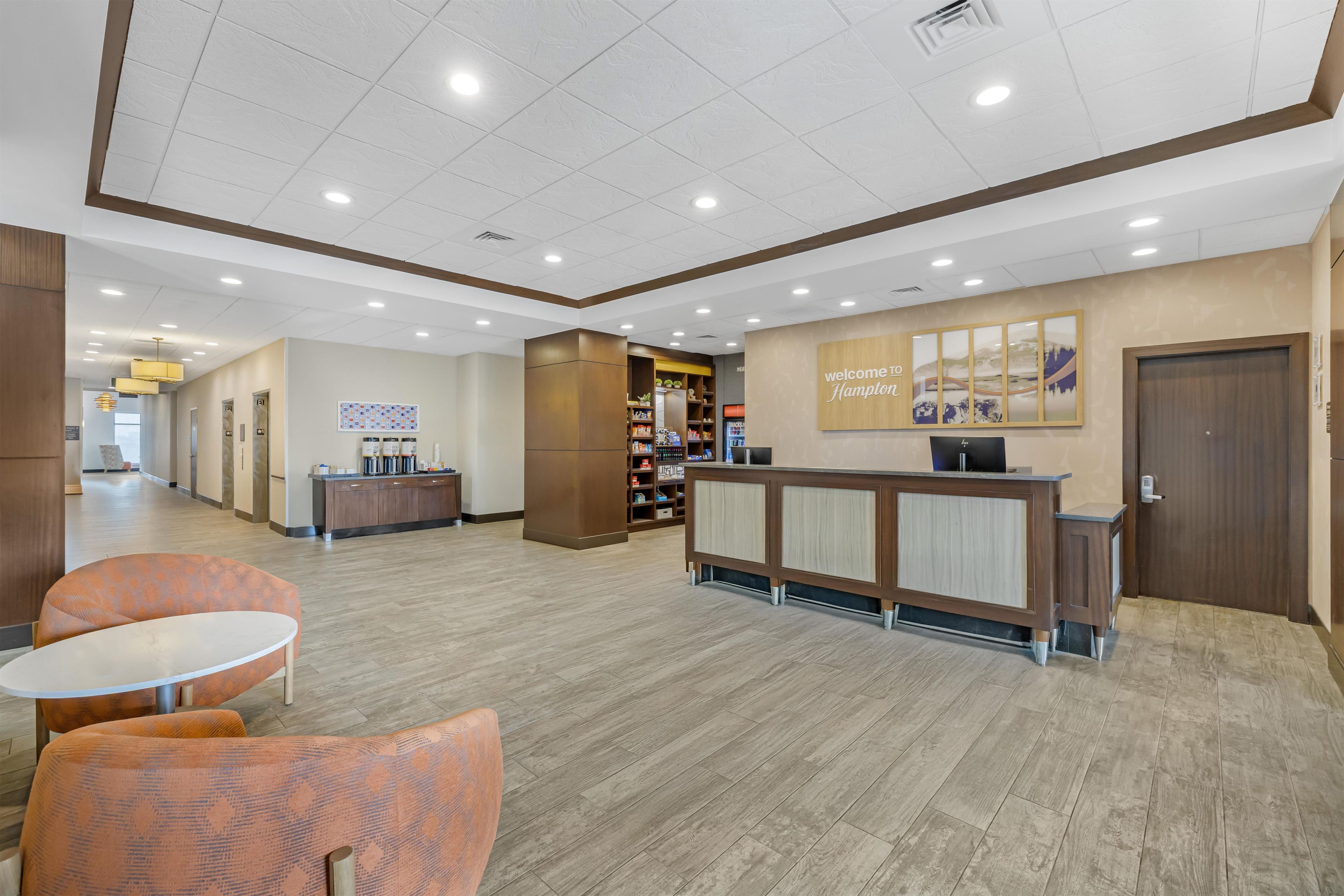 A reception area with a wooden reception desk, a coffee station, and a seating area with orange chairs.