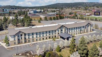 A large hotel with multiple floors, a parking lot, and a view of a hilly landscape in the background.