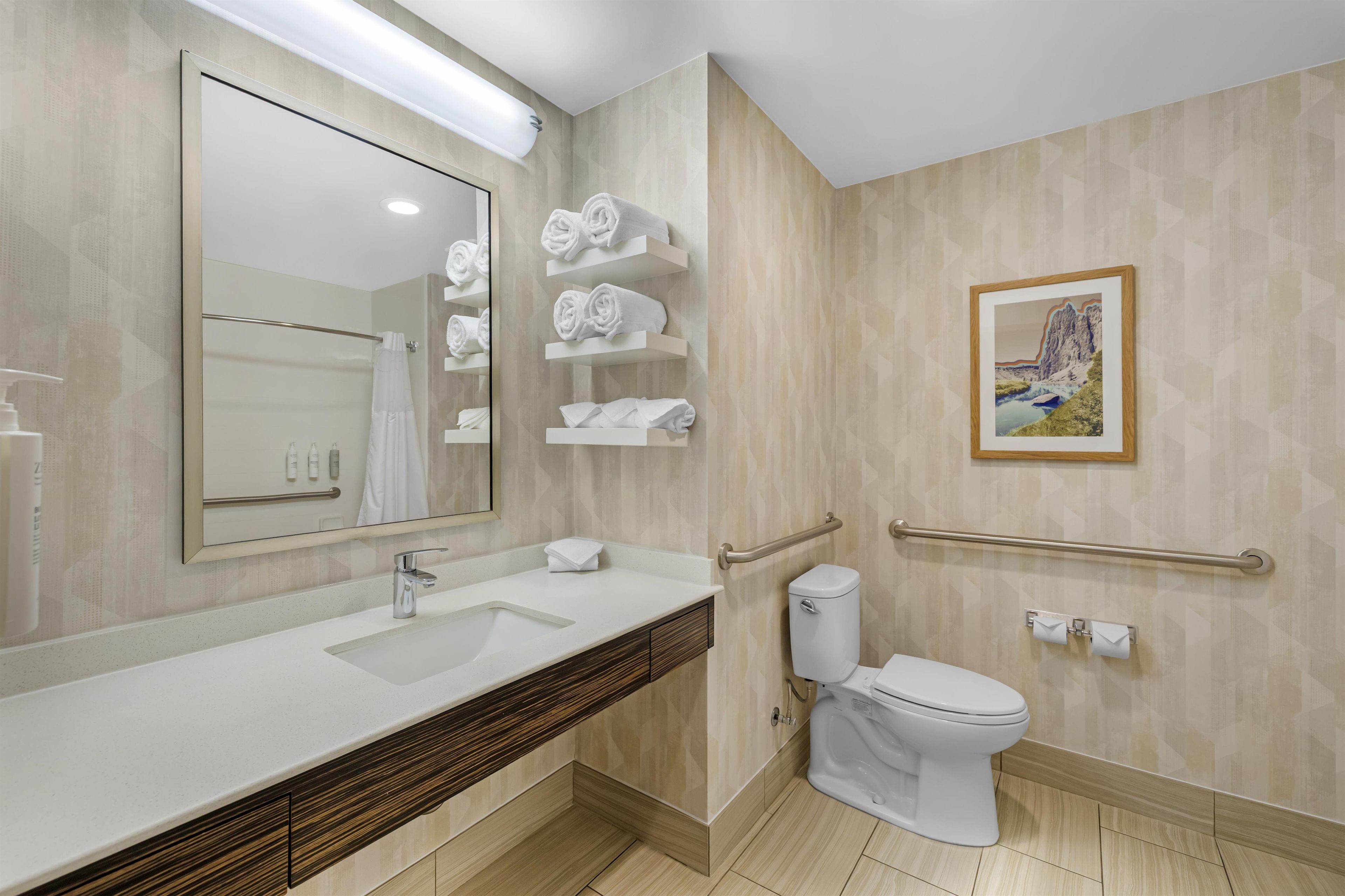 A modern bathroom with a large mirror, a sink, a toilet, and towel racks.