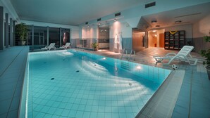 An indoor swimming pool with clear water, surrounded by lounge chairs and a sunbed. - Maximilian Lifestyle Resort (Loucen)