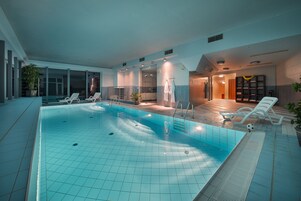 Piscina interna com água cristalina, rodeada por espreguiçadeiras e um solário.