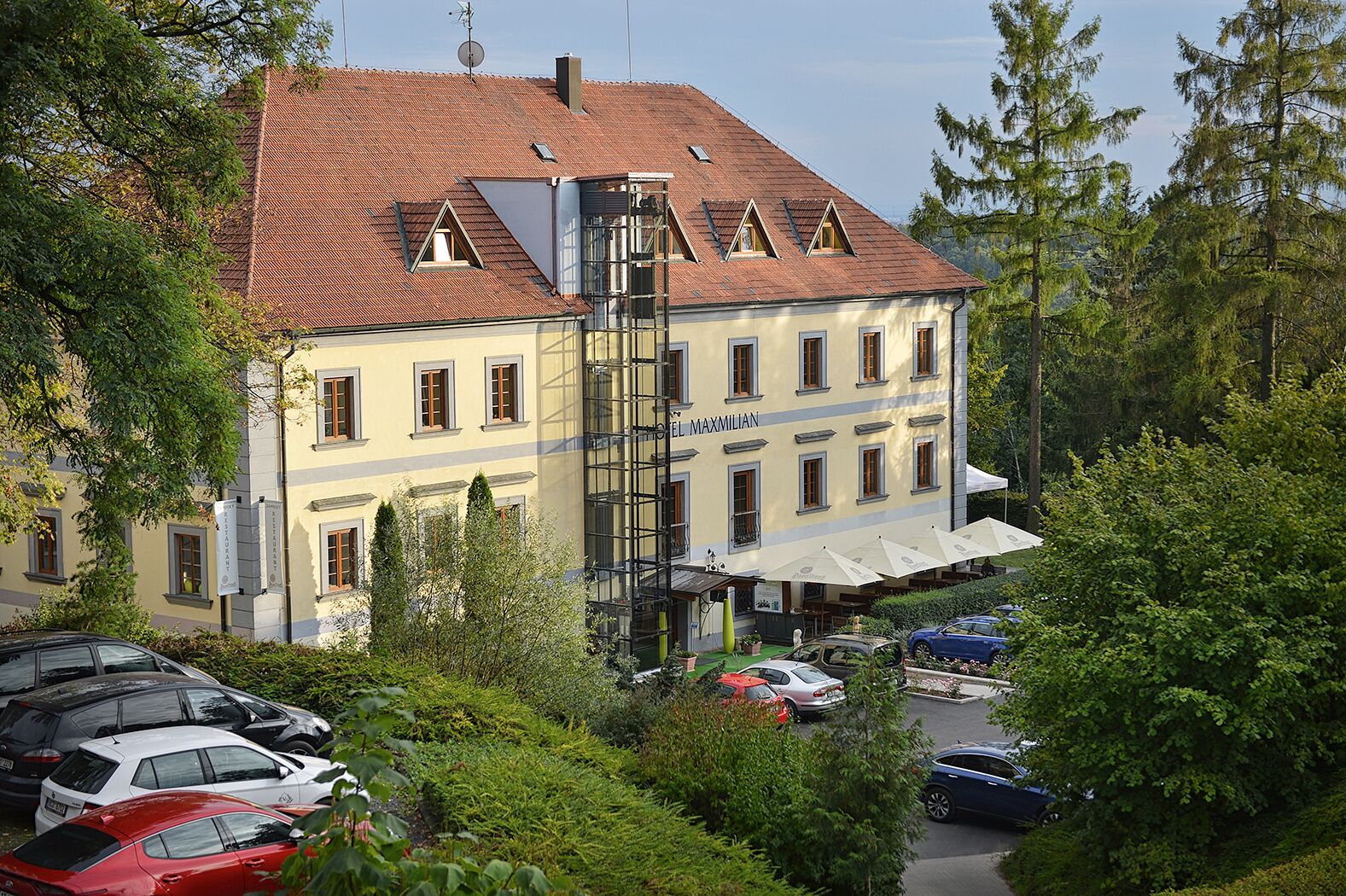 A building with a red-tiled roof, multiple windows, and a sign reading "Hotel Maximilian".