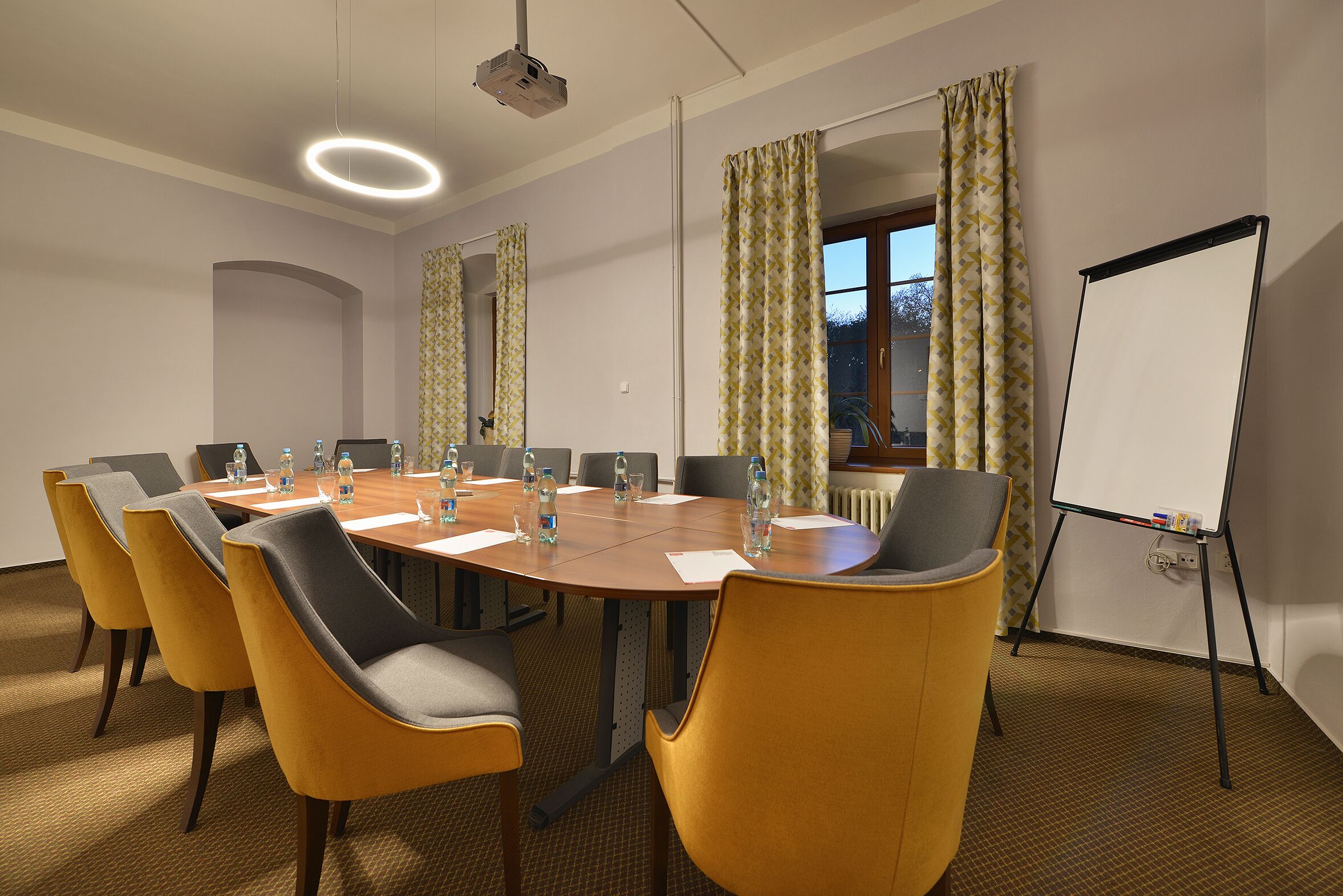 Une salle de conférence équipée d’une grande table, de chaises jaunes, d’un tableau blanc et d’un projecteur.