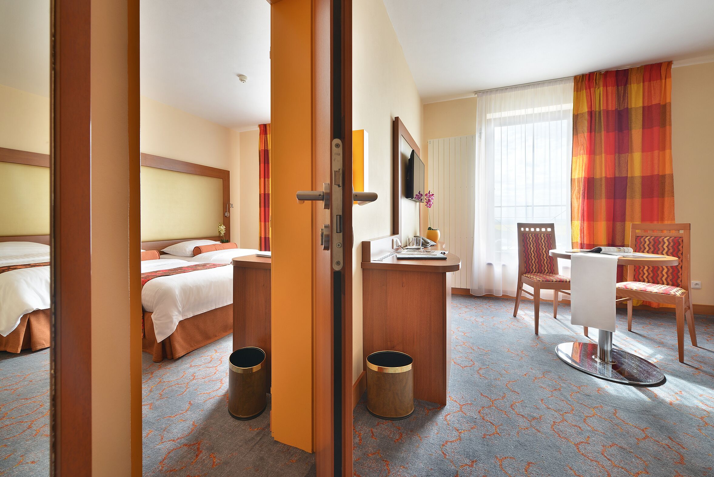 Een hotelkamer met een bed, een bureau, een stoel, een televisie en een raam met gordijnen.