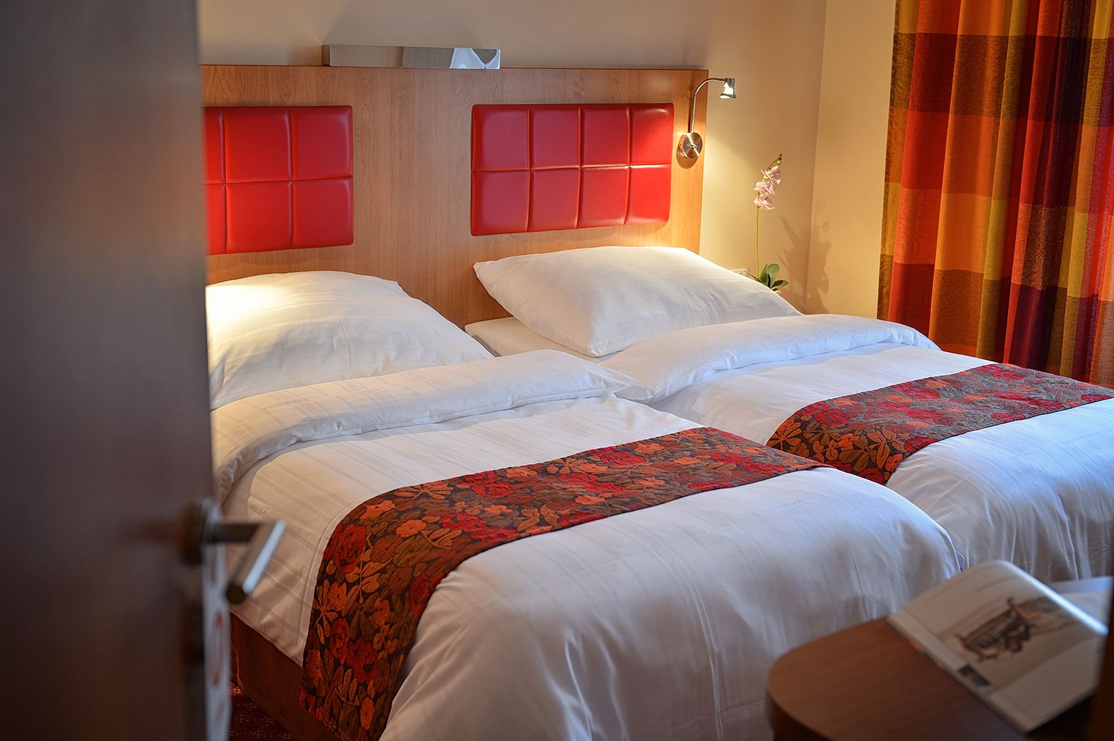 A hotel room with two beds, each with white linens and red headboards.
