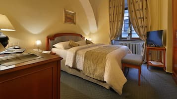 A hotel room with a bed, a desk with a lamp, a television, and a window with curtains.