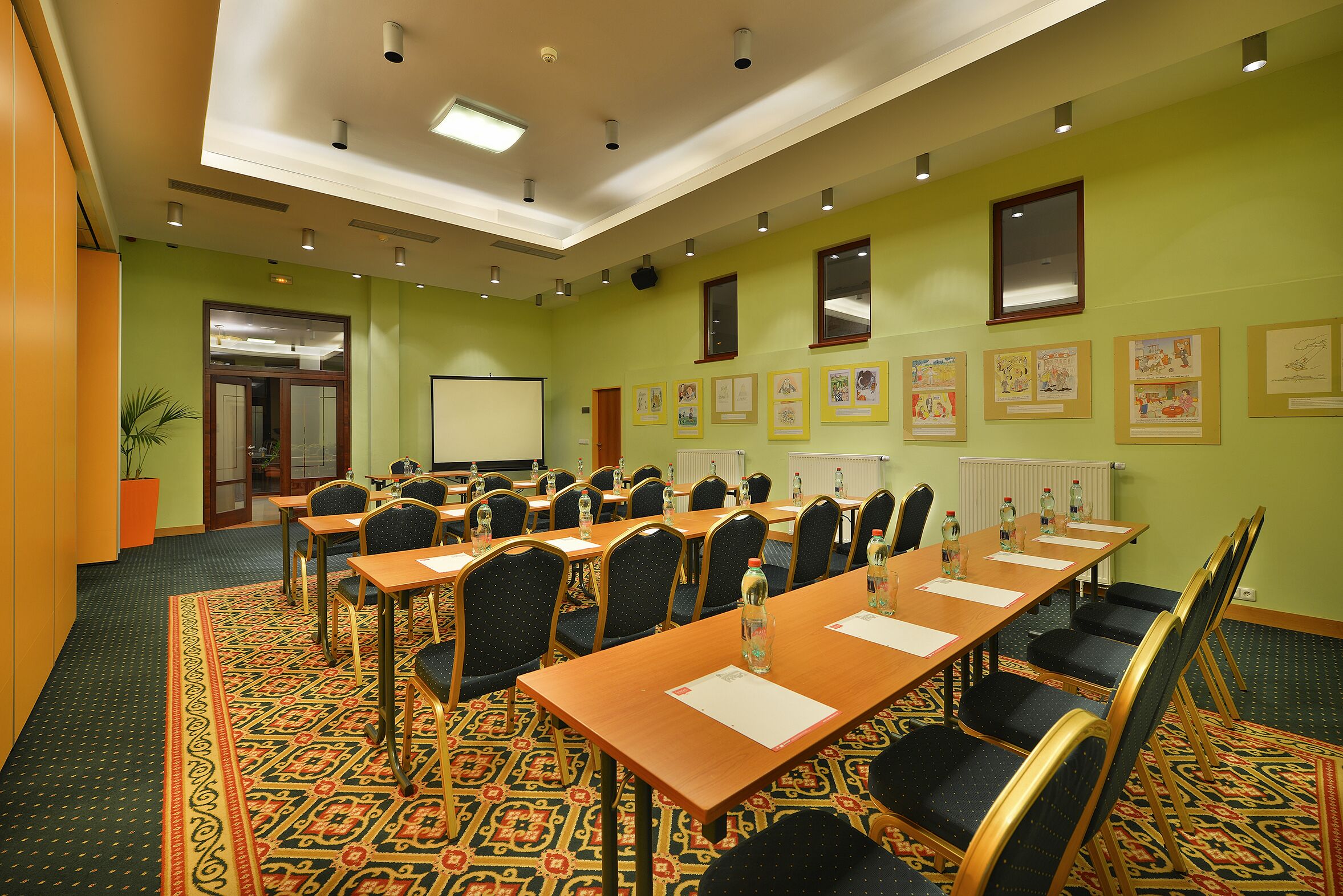 Una sala conferenze con lunghe tavolate, sedie e uno schermo per proiezioni.
