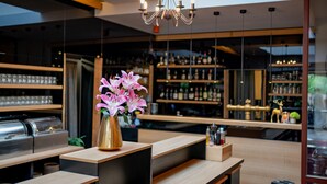 A modern bar area with a wooden counter, a chandelier, and shelves stocked with bottles. - Maximilian Lifestyle Resort (Loucen)
