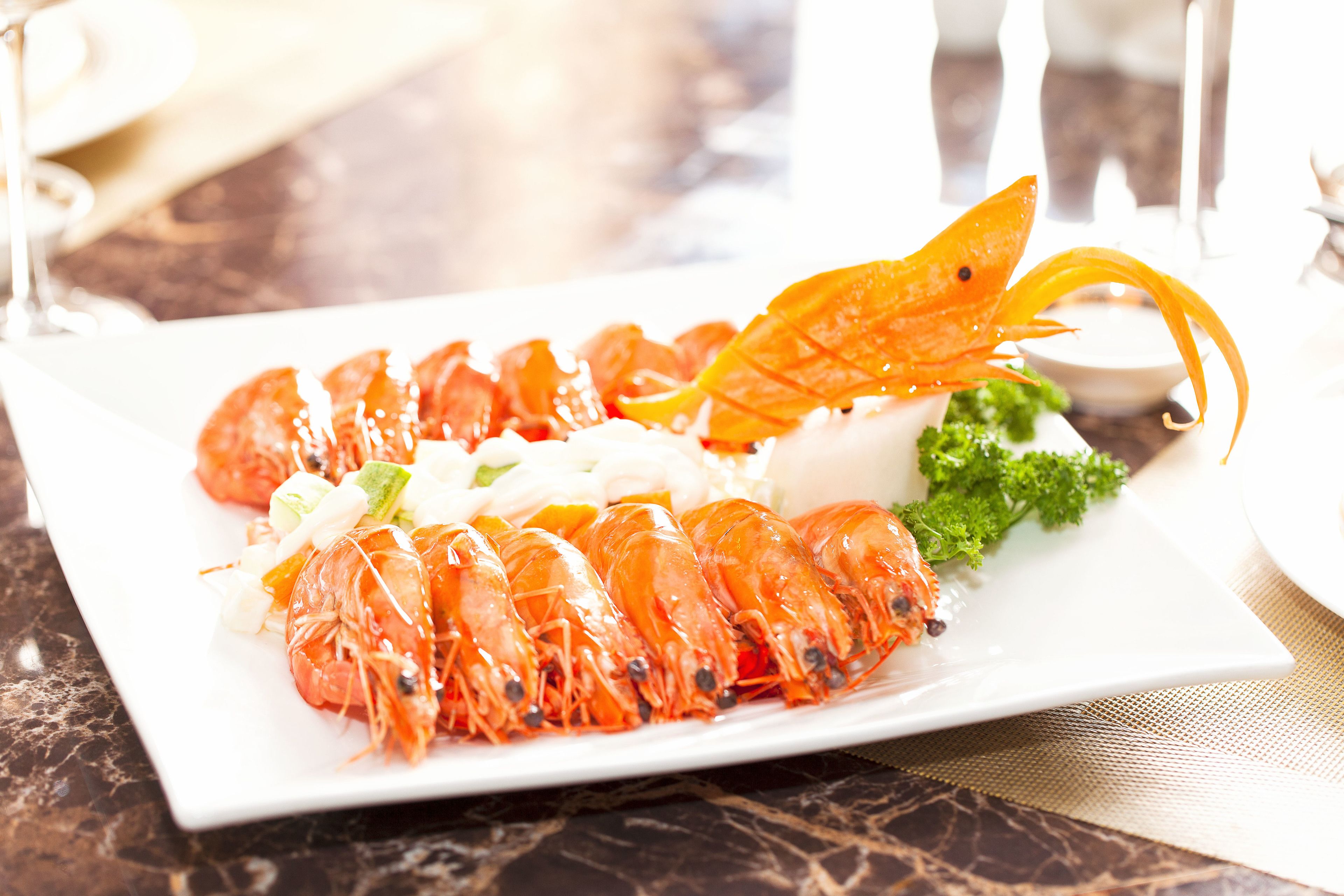 A plate of cooked shrimp with a garnish of orange leaves and green herbs, served on a white rectangular plate.