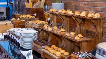 A buffet with various baked goods and pastries displayed on wooden stands against a brick wall.