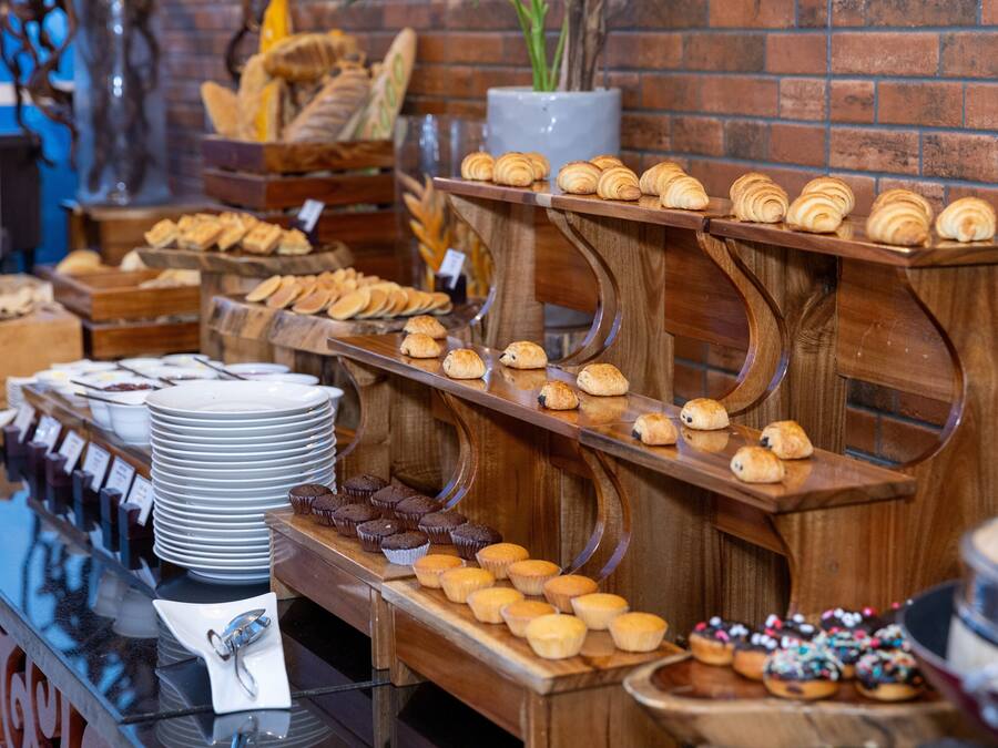 A buffet with various baked goods and pastries displayed on wooden stands against a brick wall.