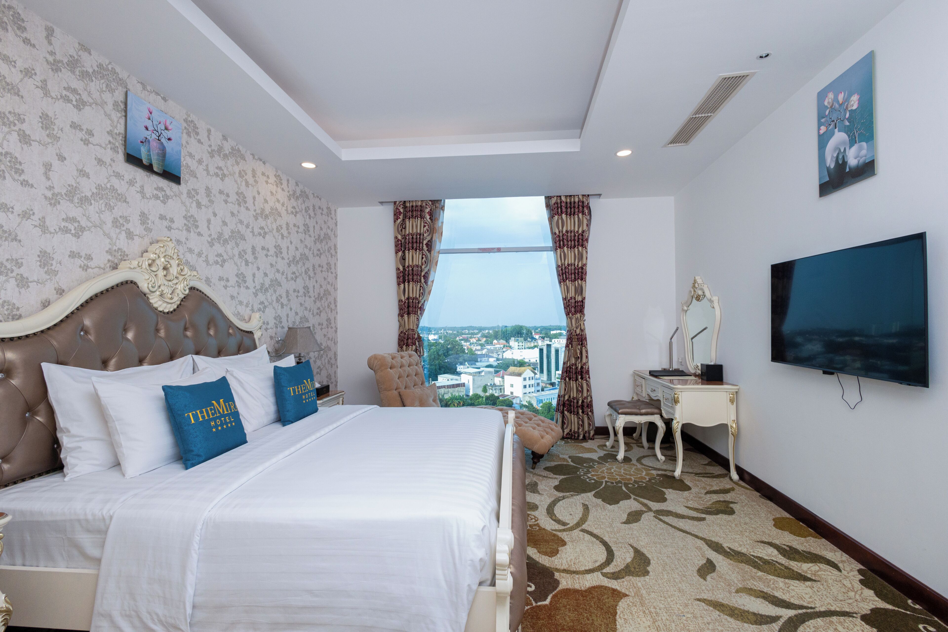 A hotel room with a large bed, a desk, a chair, and a TV.