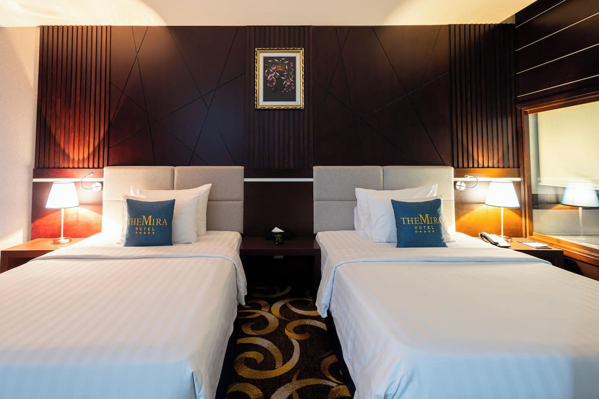 Une chambre d’hôtel avec deux lits, un mur lambrissé en bois foncé, un tableau encadré et une moquette à motifs.