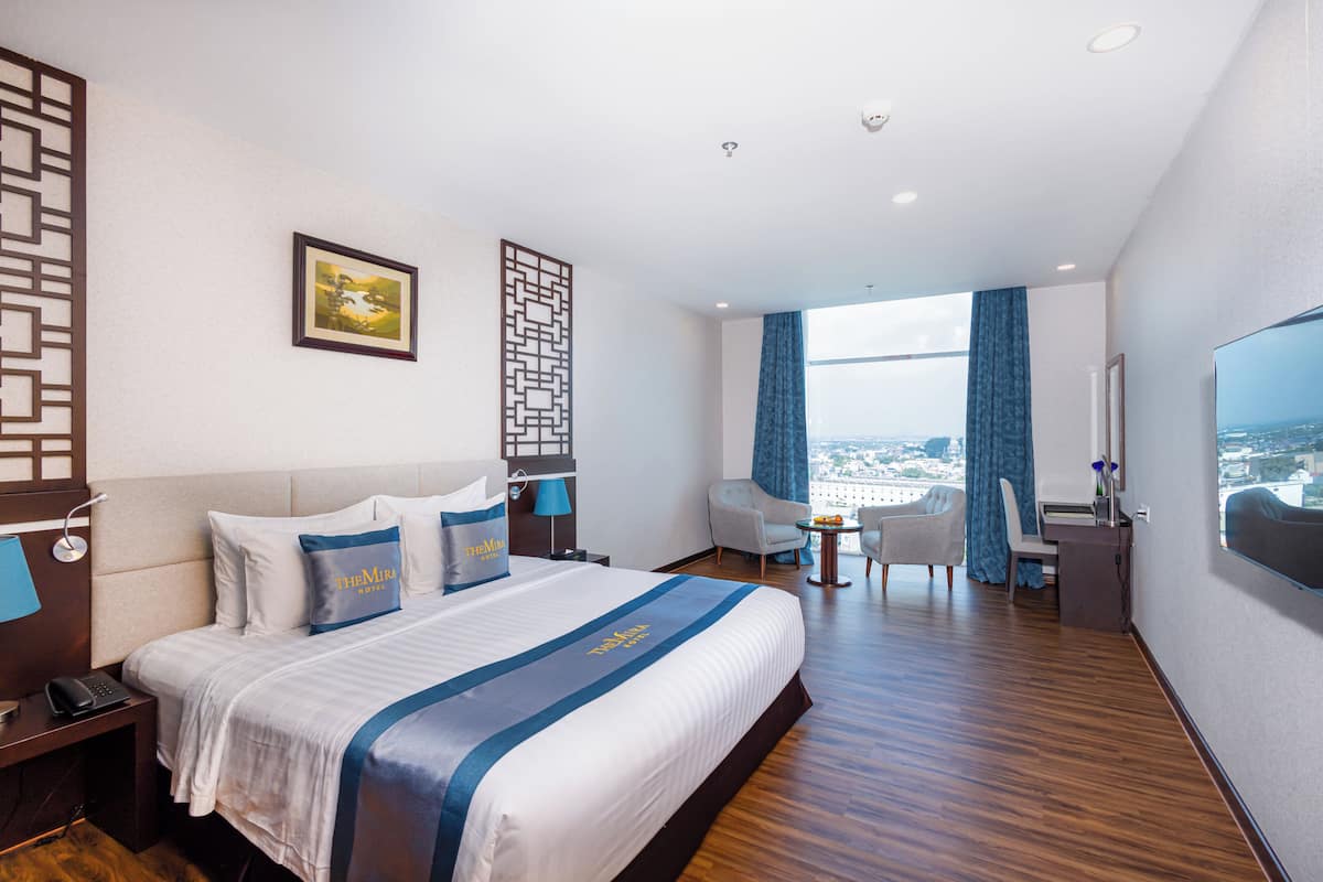 Une chambre d’hôtel avec un grand lit, un bureau, une chaise et une vue sur la ville.
