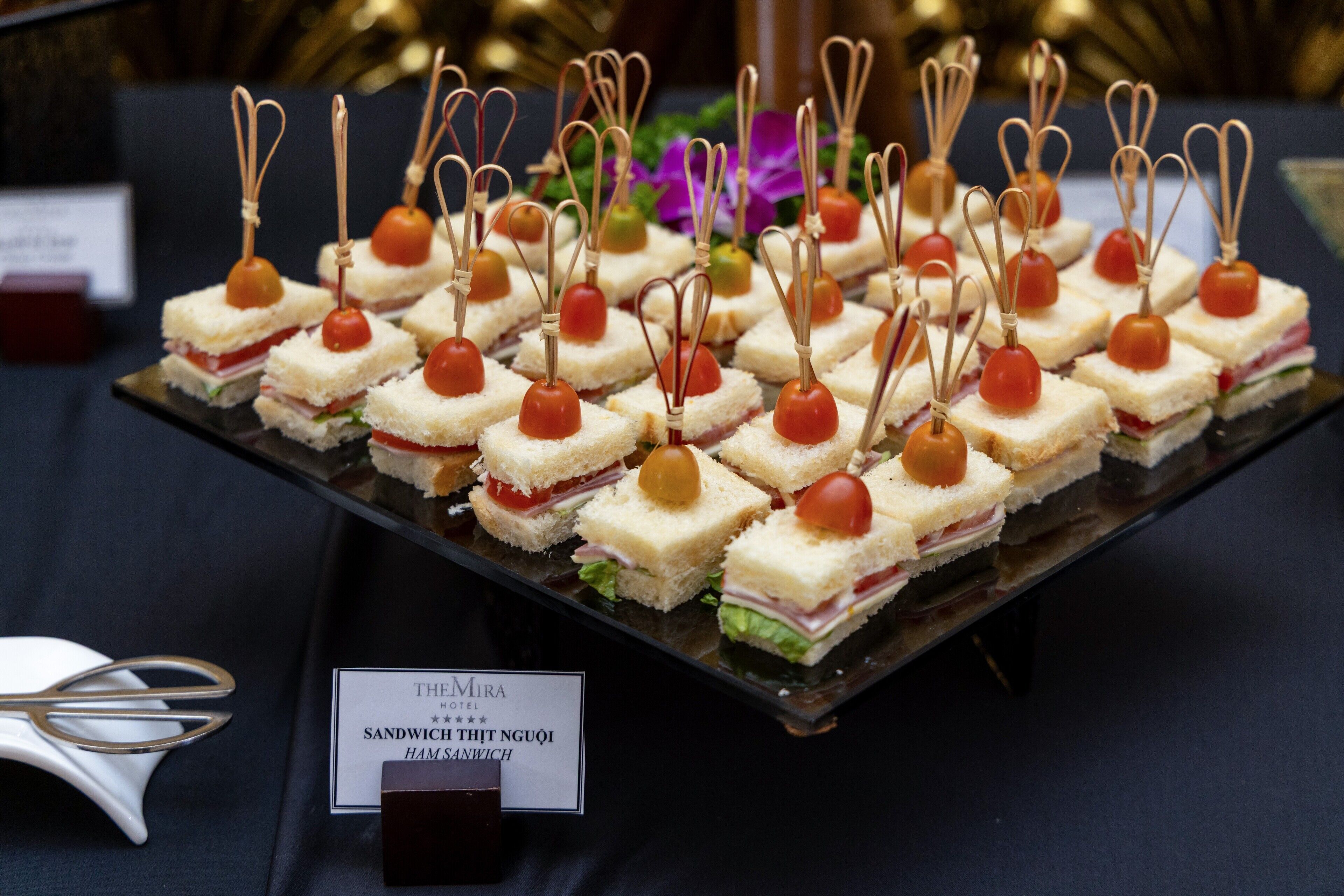 A display of sandwiches with cherry tomatoes and toothpicks, arranged on a black tray.