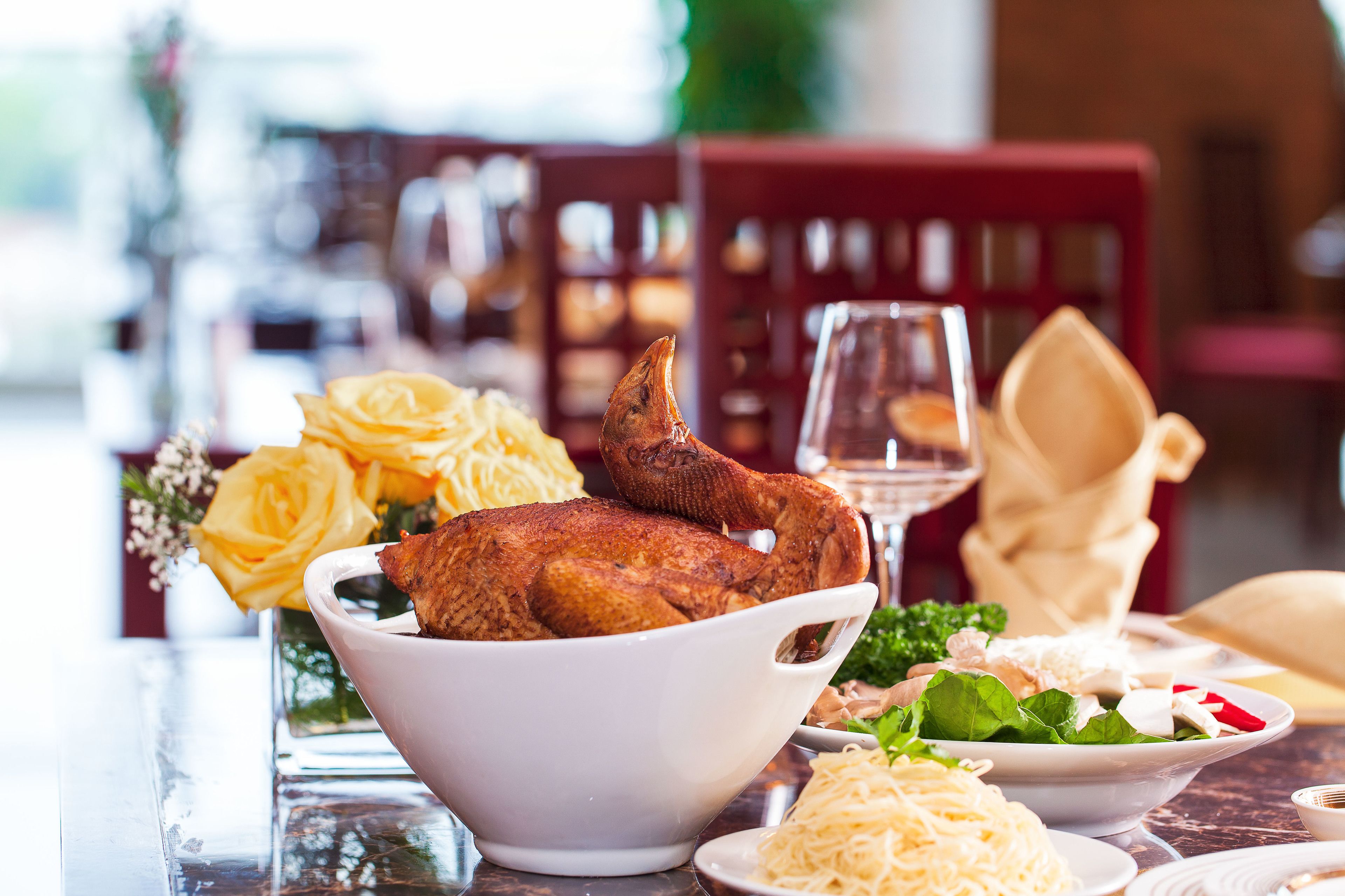 A dining table with a roasted chicken, yellow roses, and various dishes.