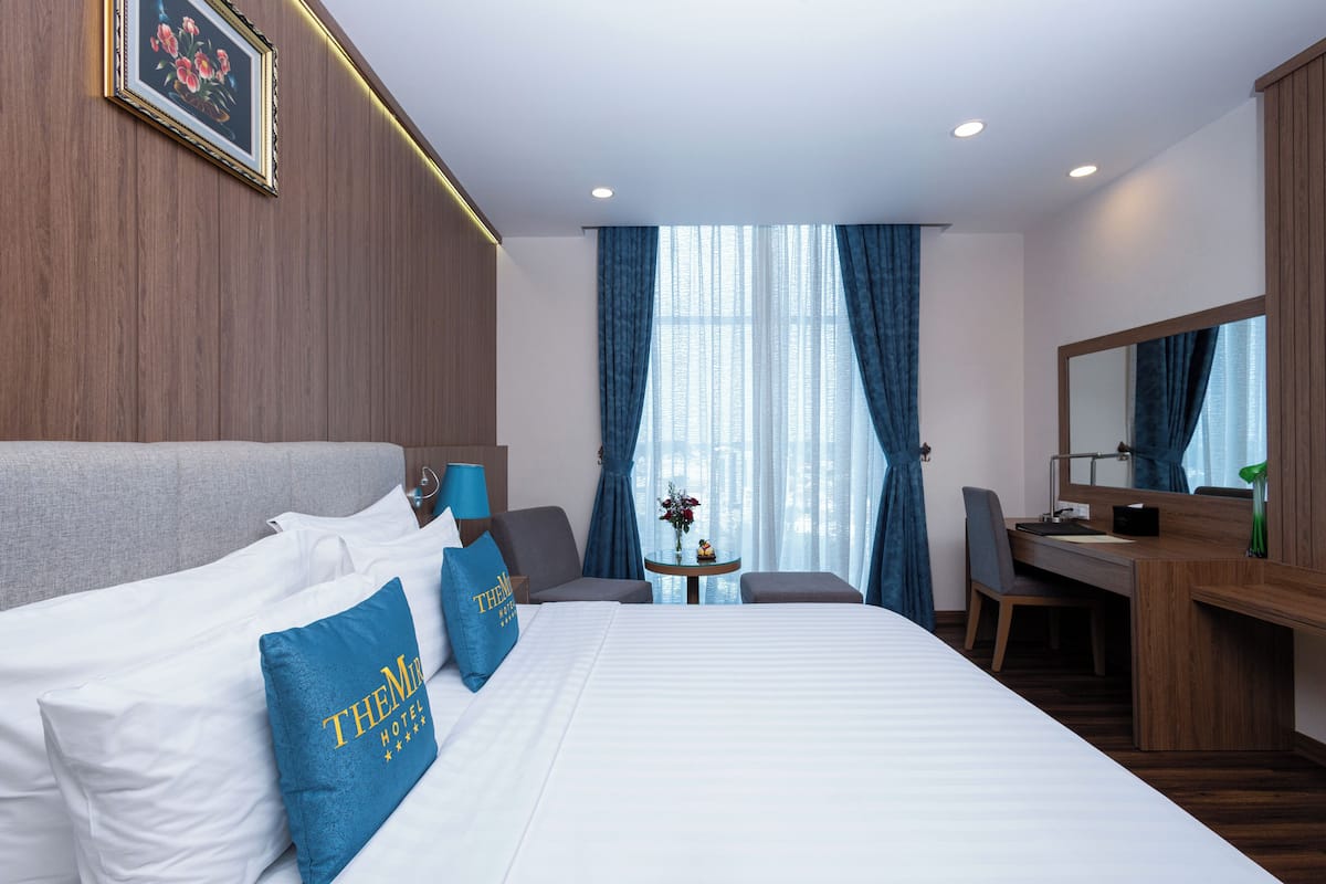 Une chambre d’hôtel avec un grand lit, un bureau, une chaise, une petite table avec un vase et un grand miroir.