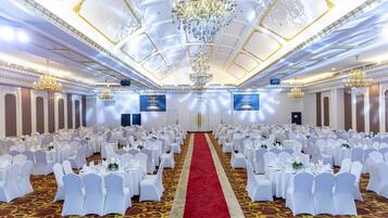 A banquet hall with round tables, white chairs, a red carpet, and chandeliers.