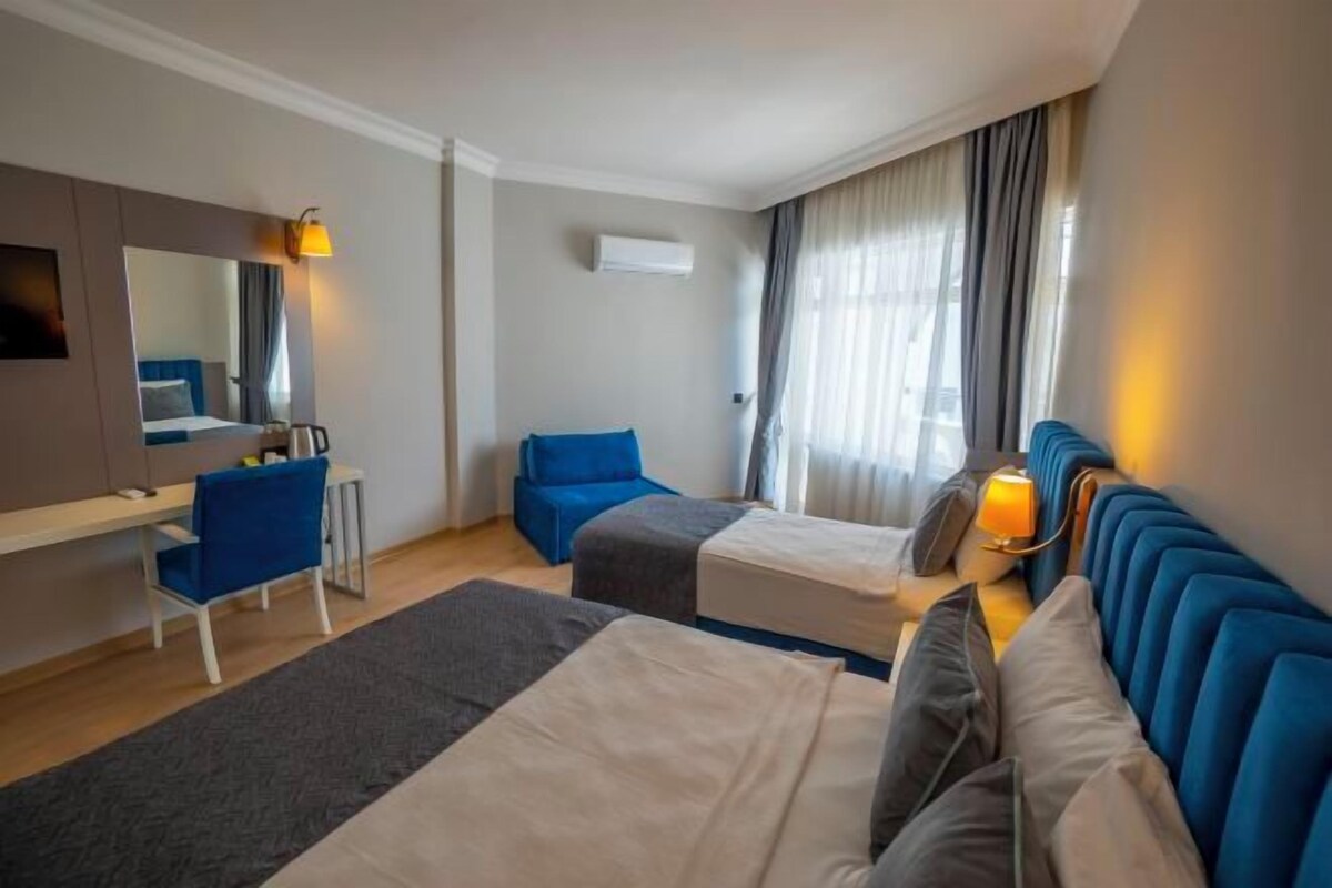 A hotel room with two single beds, a desk with a chair, a TV, and a window with curtains.