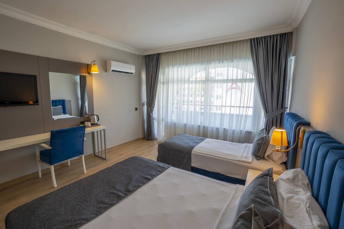 A hotel room with two beds, a desk, a chair, a TV, and a window with curtains.