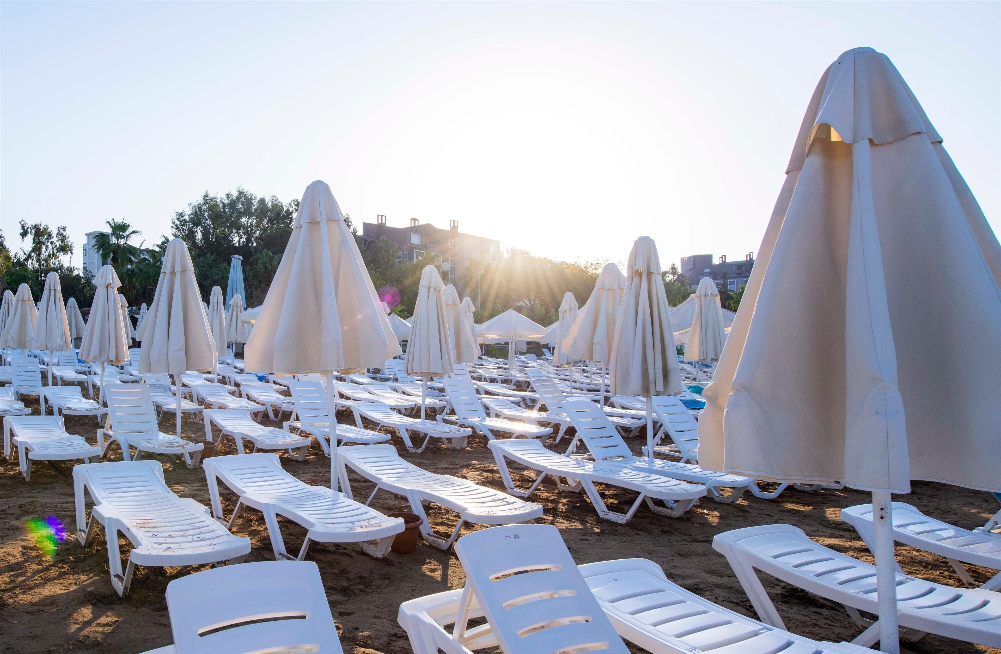 Une plage bordée de rangées de transats blancs et de parasols, disposés selon un motif harmonieux.