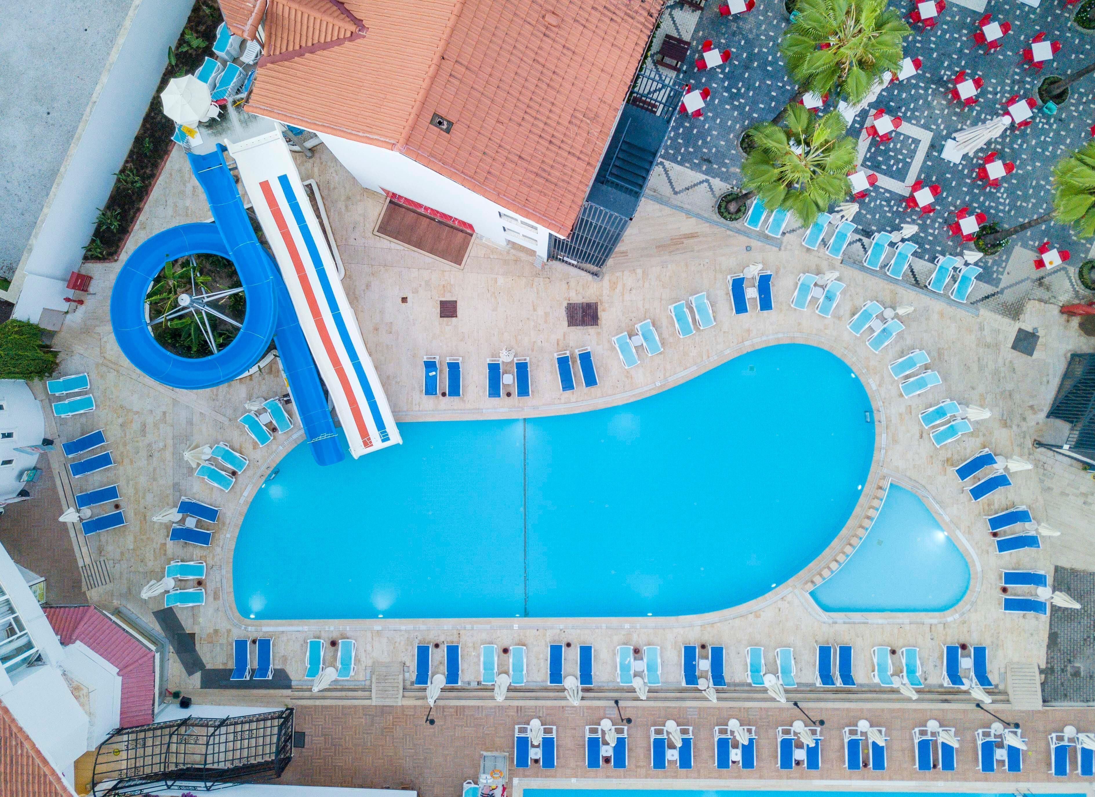An aerial view of a hotel with a large swimming pool, multiple lounge areas, and a slide.