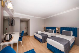 A hotel room with two beds, a desk, a chair, a coffee maker, and a TV.