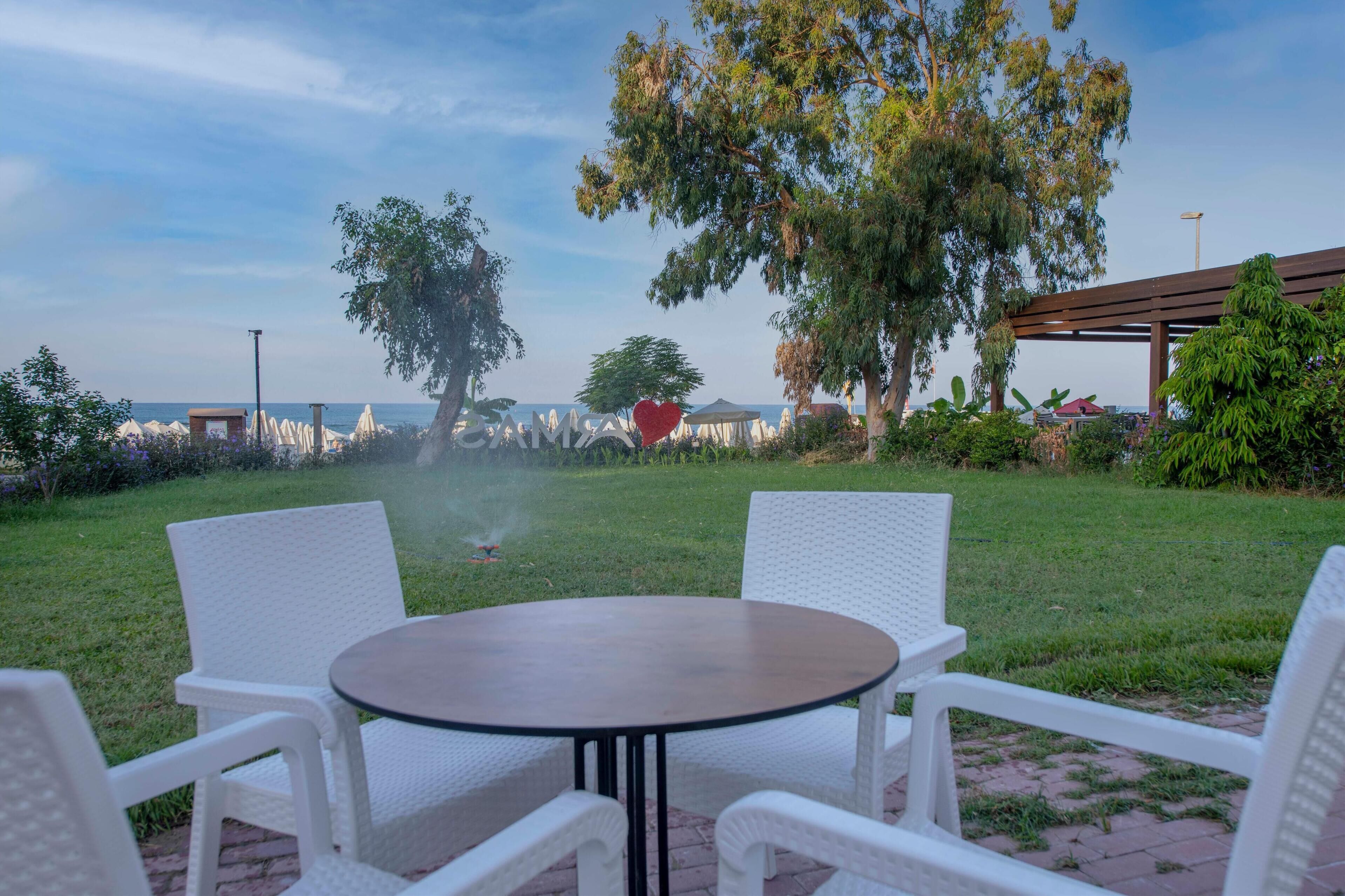 Un patio con sillas de mimbre blanco y una mesa redonda, con vistas a una zona verde y el mar.