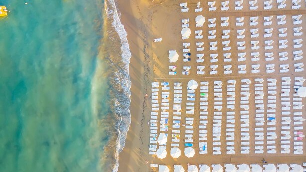 An aerial view of a beach with rows of white sun loungers and umbrellas, a sandy shore, and gentle waves. - Armas Bella Sun - All Inclusive (Manavgat)
