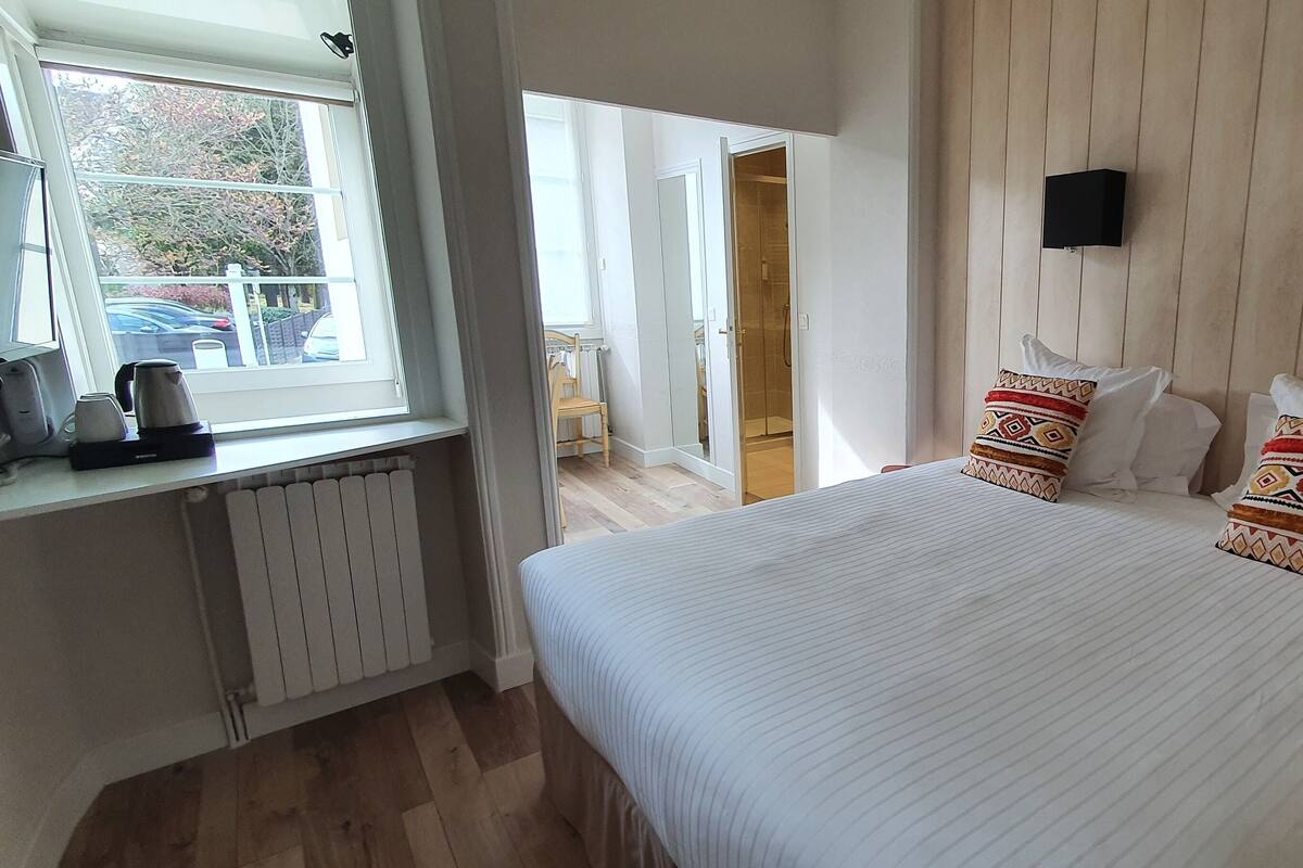 Une chambre à coucher avec un grand lit, deux tables de chevet, une fenêtre donnant sur l’extérieur et un radiateur.
