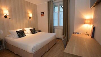 A hotel room with a large bed, bedside lamps, a window with curtains, and a wooden desk.