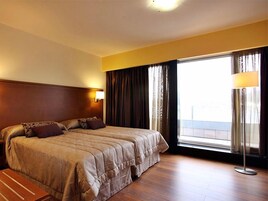 Habitación de hotel con una cama grande, una mesita de noche, una lámpara y un ventanal con cortinas.