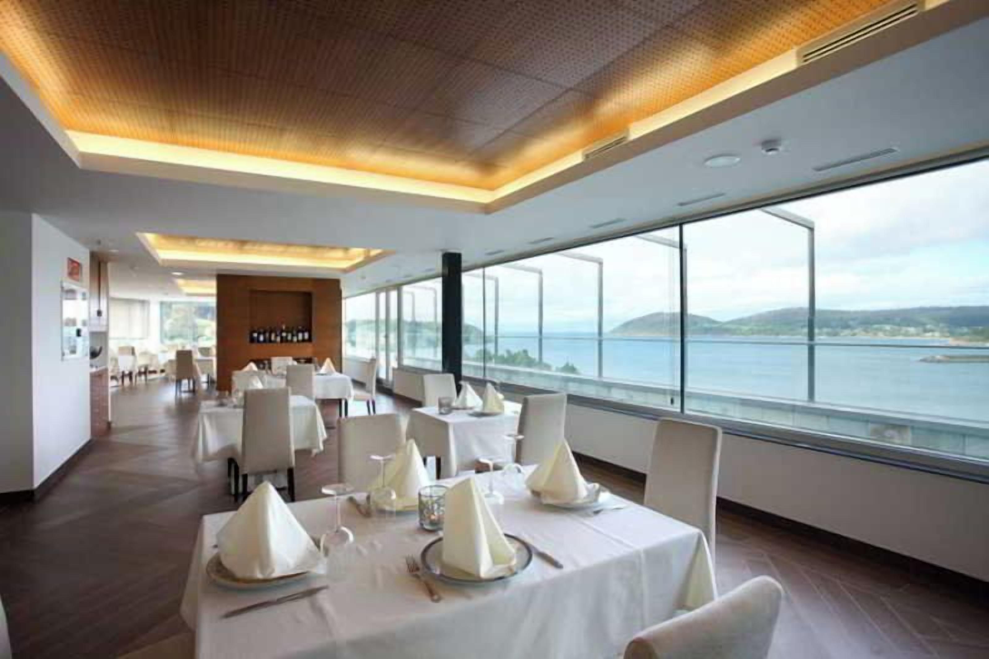 Ein Essbereich mit gedeckten Tischen, Blick auf das Meer und modernes Interieur.