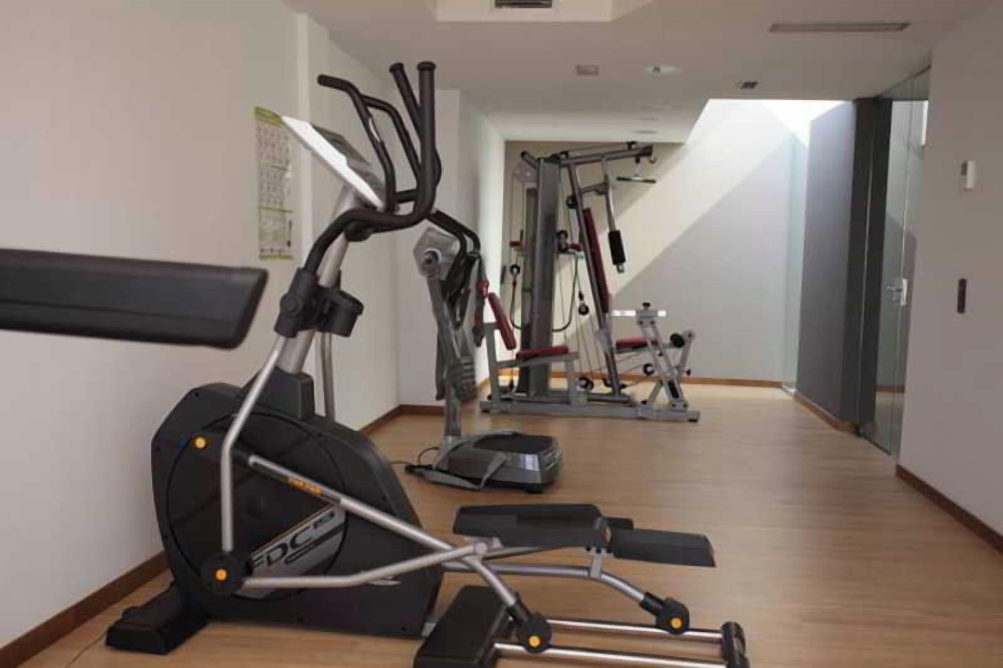 Un gimnasio con equipo de ejercicio, incluyendo una elíptica, una cinta de correr y una bicicleta estática.