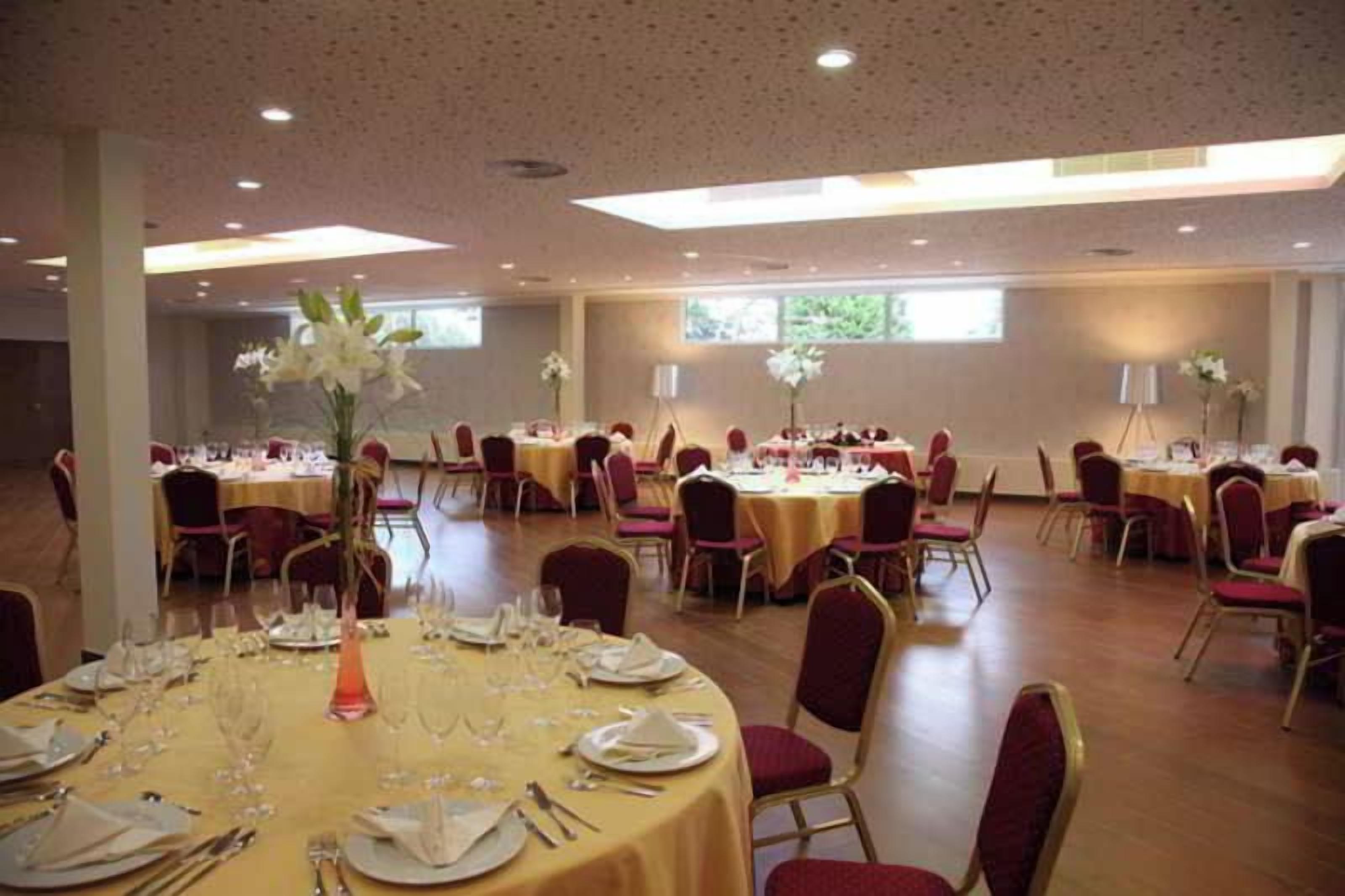 Un salón de banquetes con mesas redondas dispuestas para comer, sillas y centros de mesa con flores.
