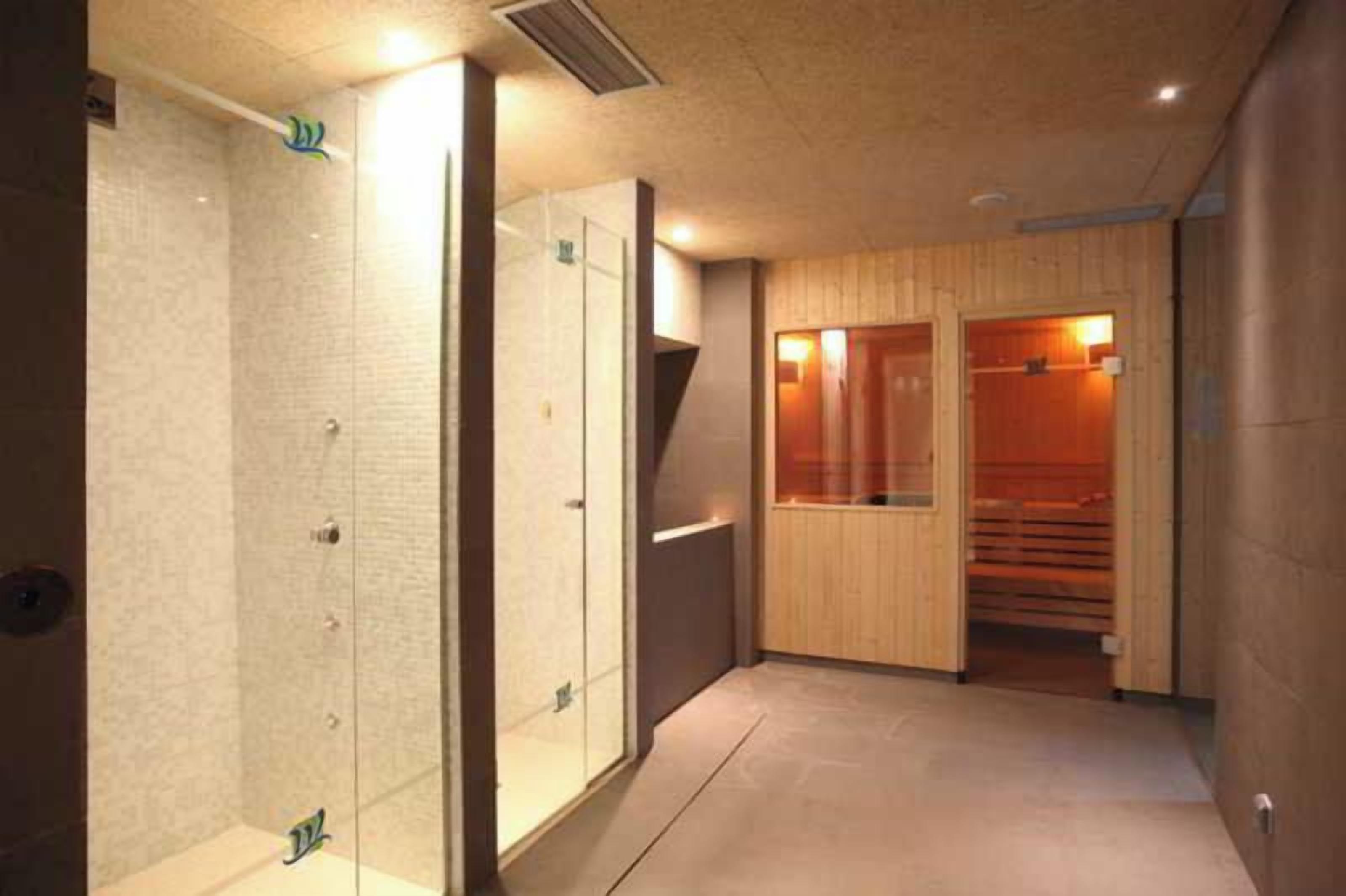 Un couloir donnant accès à un espace sauna, à une douche à parois de verre et à un sauna en bois.