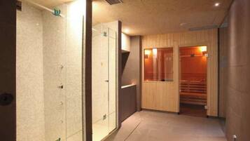 Un couloir donnant accès à un espace sauna, à une douche à parois de verre et à un sauna en bois.