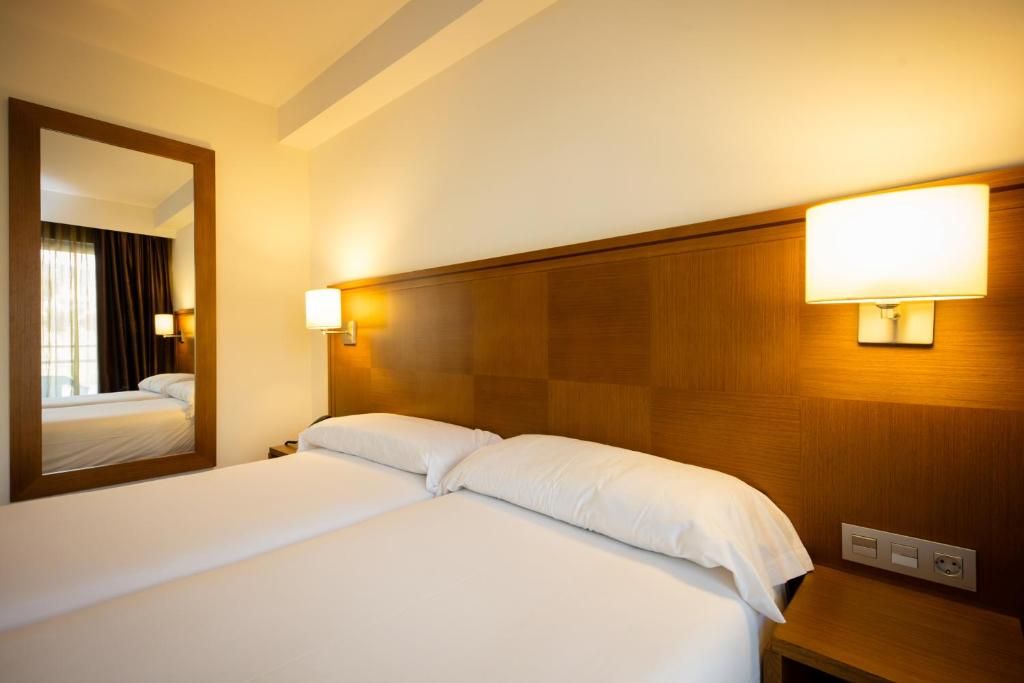 A hotel room with two beds, a large mirror, and wall-mounted lamps.
