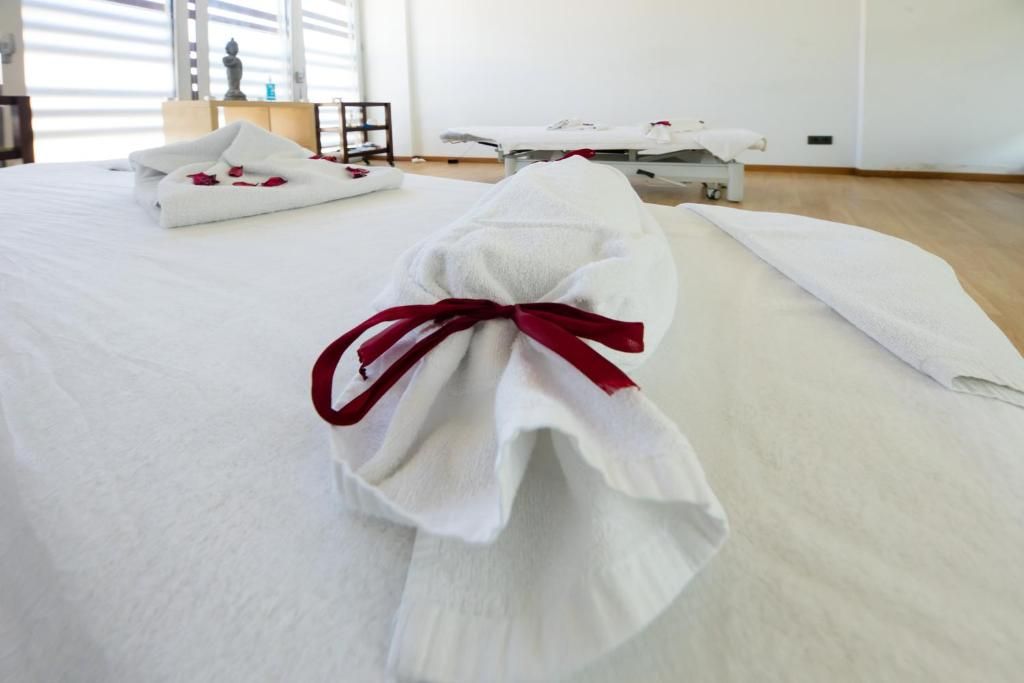 A hotel room with a neatly made bed, a massage table, and a small bedside table with a lamp.