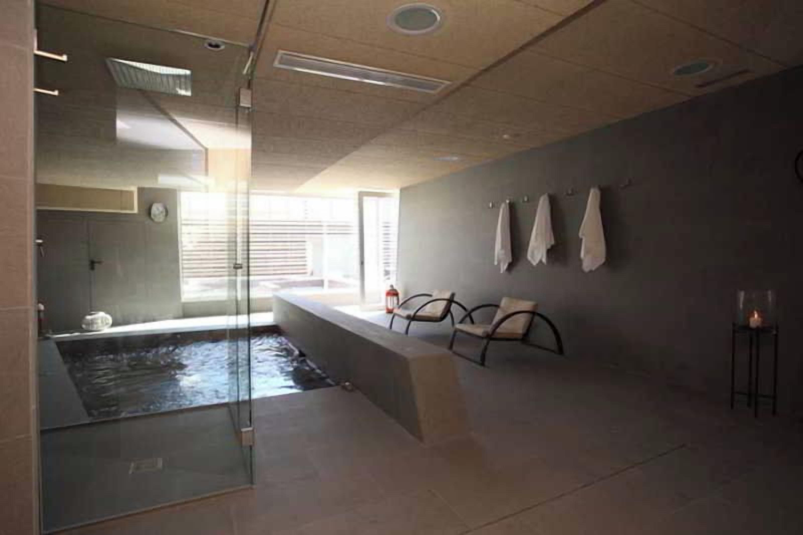 A modern bathroom with a glass-enclosed shower, a bathtub, and a seating area with towels.