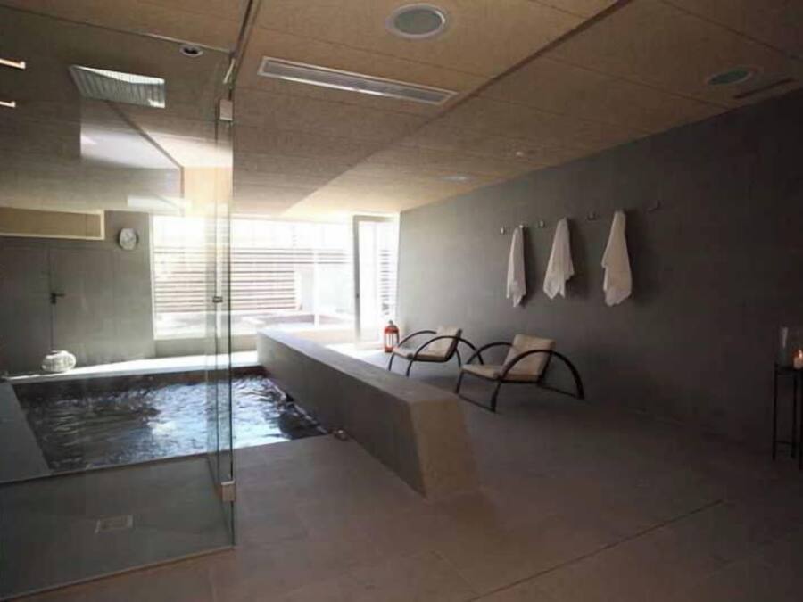 A modern bathroom with a glass-enclosed shower, a bathtub, and a seating area with towels.