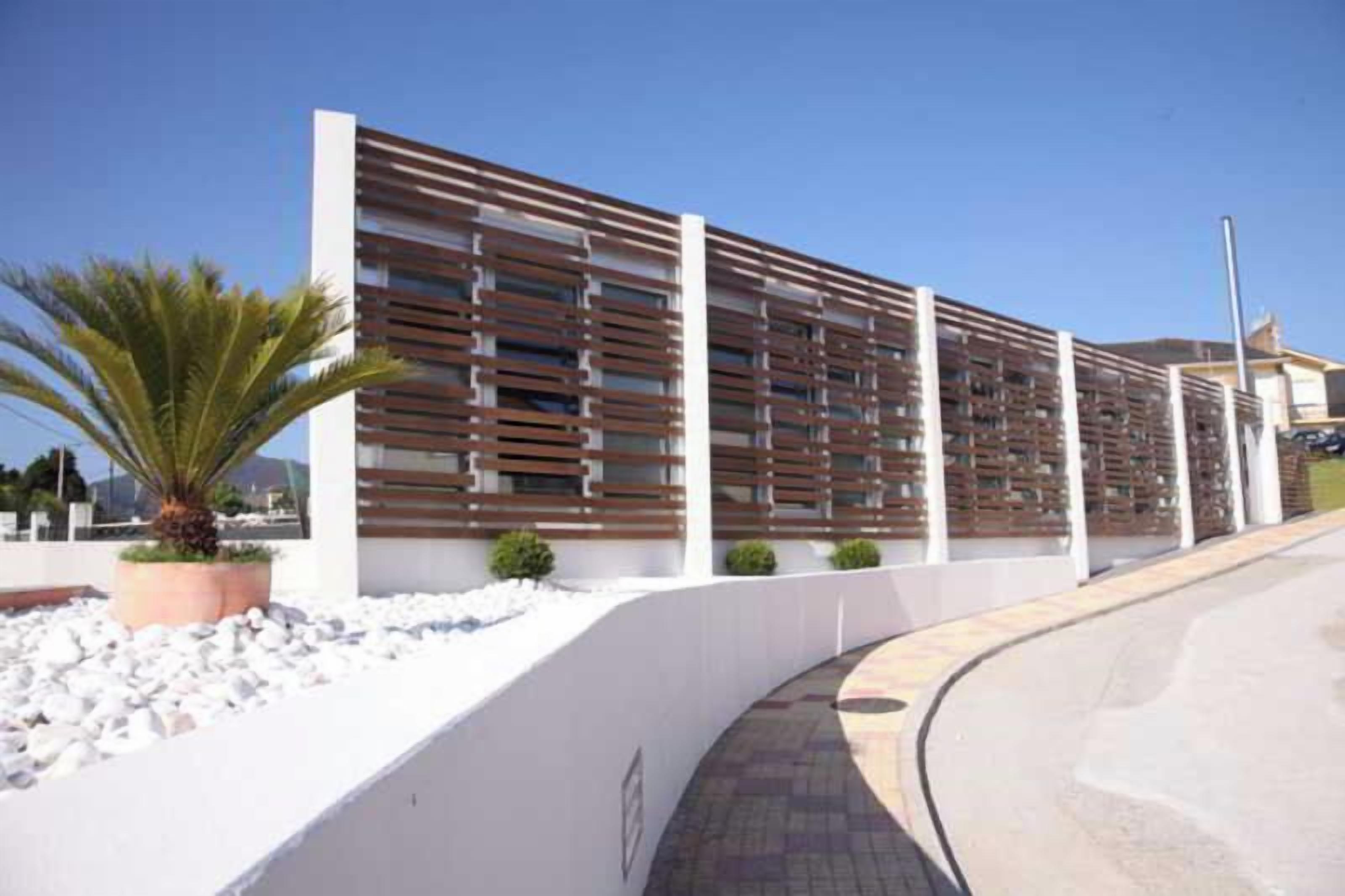 Un edificio moderno con fachada blanca, un sendero curvo y una palmera.