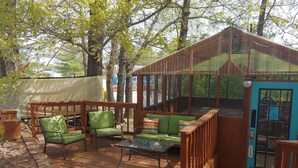 A covered outdoor seating area with green chairs and a sofa, a wooden deck, and a blue door with a sign. - Shady Acre Inn and Suites (Branson West)