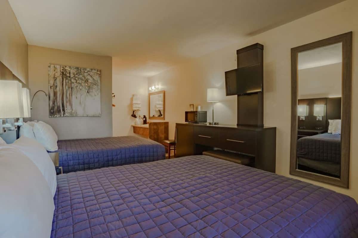 A hotel room with two beds, a desk, a dresser, a mirror, and artwork on the wall.
