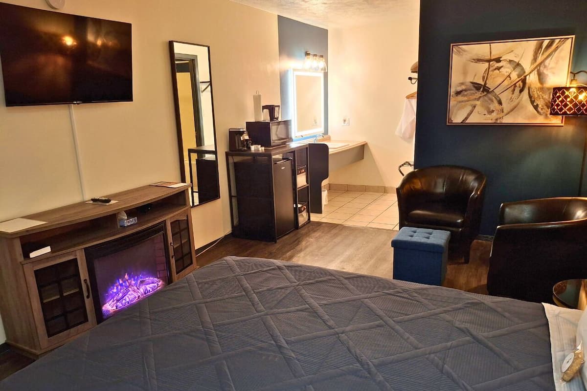 A hotel room with a bed, a TV, a mirror, a desk, a chair, and a fireplace.